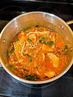 a pot filled with pasta and spinach soup on top of an oven burner