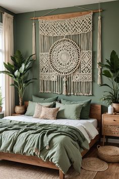 a bed with green sheets and pillows in front of a large macrame wall hanging