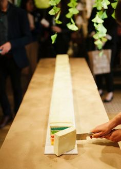 a woman cutting into a piece of cake on top of a wooden table with people in the background