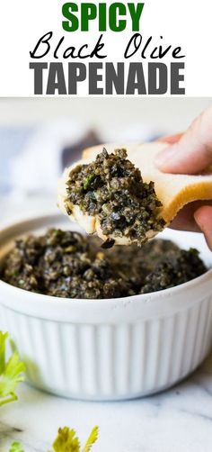 a hand holding a piece of bread over a bowl of black olive tapenade