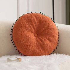 an orange round pillow sitting on top of a white couch next to a small book