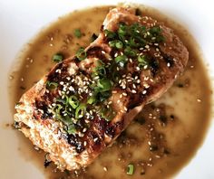 a white plate topped with meat covered in sauce and garnished with green onions