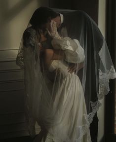 a bride and groom kissing under a veil in front of a window with sunlight streaming through it