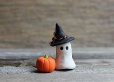 a small white ghost with a black hat next to a fake pumpkin on the ground