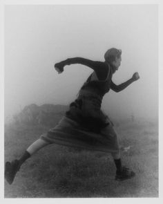 a woman is running in the fog with her arms spread out and legs bent forward