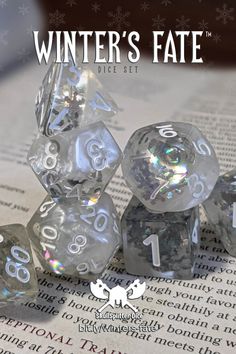 the winter's fate dice set is shown on top of an open book with snowflakes