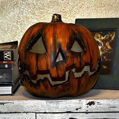 a carved pumpkin sitting on top of a wooden shelf next to a book and framed photograph