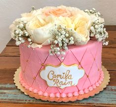 a pink and white cake with flowers on top sitting on a wooden table next to a wall