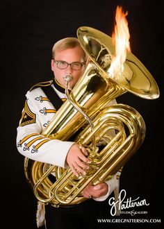 a man with glasses holding a large brass instrument in his right hand and flames coming out of it