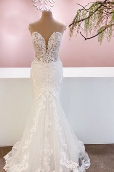 a white wedding dress on display in front of a pink wall with flowers and branches