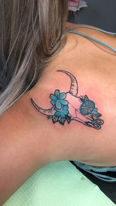 a woman's upper back tattoo with flowers and a cow skull on her shoulder