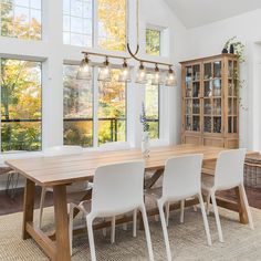 a dining room table with white chairs in front of large windows