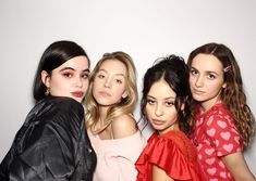 four girls are posing for the camera in front of a white wall with hearts on it