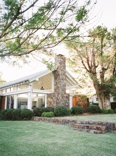 a house that is in the grass with trees and bushes around it's corner