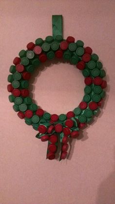 a green and red wreath made out of plastic bottle caps hanging on a pink wall