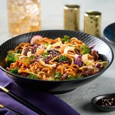 a bowl filled with noodles, broccoli and other vegetables on top of a table