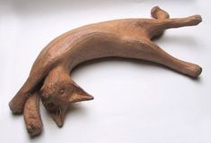 an animal made out of wood laying on top of a white surface with one foot up