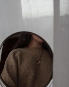 a woman's reflection in a mirror with a gold necklace on her left shoulder