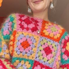 a woman wearing a multicolored crocheted sweater and earrings smiling at the camera