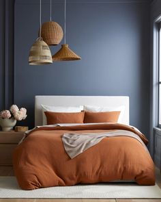 a bed with two lamps hanging from it's sides and an orange comforter