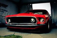 a red car is parked in a garage with its lights on and the hood up