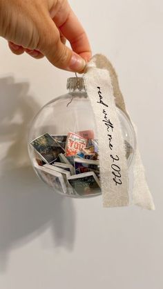 a hand is holding a glass ornament with some pictures on it and a ribbon