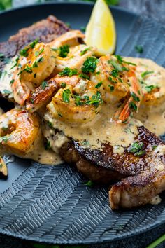 a plate topped with meat and shrimp covered in gravy next to a lemon wedge