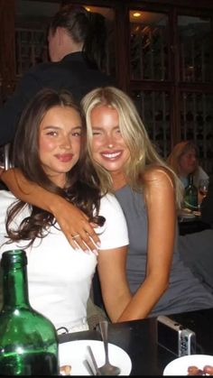 two beautiful young women hugging each other in front of a table with wine bottles on it