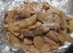 a pile of fried food sitting on top of aluminum foil covered in powdered sugar