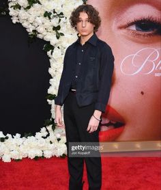 a young man standing on the red carpet at an event with flowers in front of him