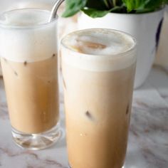 two glasses filled with drinks sitting on top of a table next to a potted plant