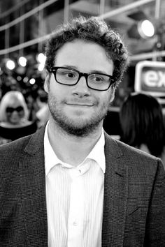 a man with glasses and a beard smiling at the camera while standing in front of a crowd