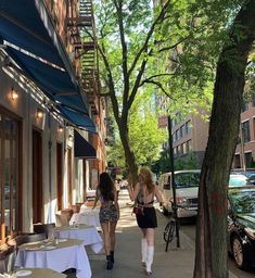 two women walking down the sidewalk in front of some tables with white tablecloths