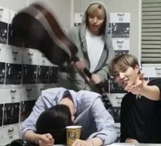 three people sitting at a table in front of stacks of books and papers with one person pointing