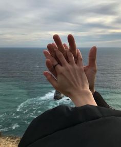 a person holding their hands up to the sky near the ocean with waves crashing in front of them