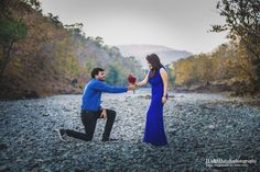 a man kneeling down next to a woman in a blue dress and holding a red rose