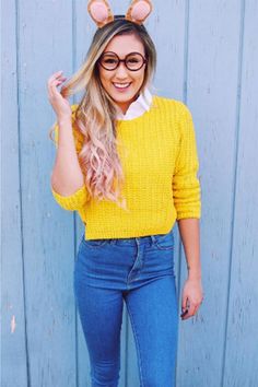 a woman wearing glasses and a yellow sweater is standing in front of a blue wall