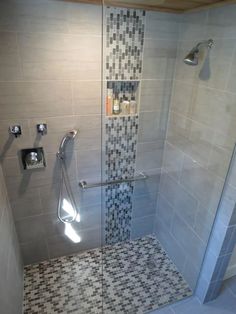 a walk in shower sitting next to a tiled wall and white tile floor with black and gray tiles on the walls