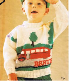 a young boy wearing a green hat and sweater with a bus on it's back