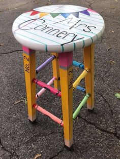 a colorful stool with writing on it sitting in the middle of an asphalt area next to a parking lot