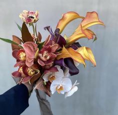 a bouquet of flowers is being held up by someone's hand in front of a wall