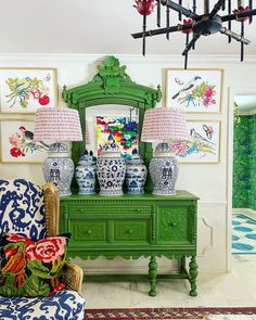 a green dresser with two lamps on top of it in front of pictures and paintings