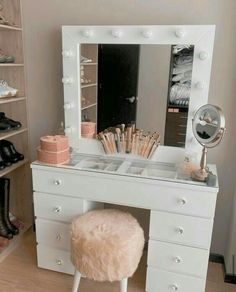 a white vanity with lights on it and a stool in front of the mirror,