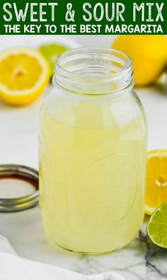 a mason jar filled with lemonade next to sliced lemons and lime wedges