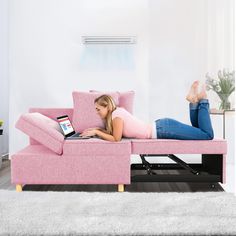 a woman laying on a pink couch using a laptop