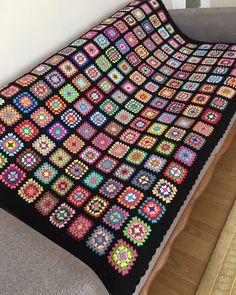 a crocheted granny blanket is sitting on a couch in front of a window