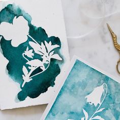 two cards with flowers on them next to some scissors and thread, one is blue and the other is green