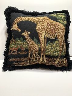 a giraffe and her baby are depicted on a decorative pillow with fringe trim