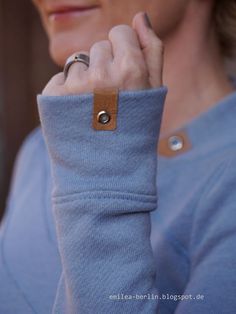 a woman wearing a blue sweater with a leather ring on her left hand and a wooden button in the middle