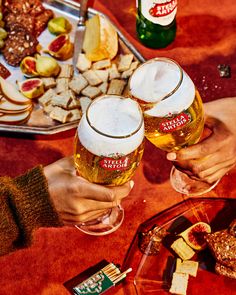 two people toasting with beer and crackers in front of food on a table